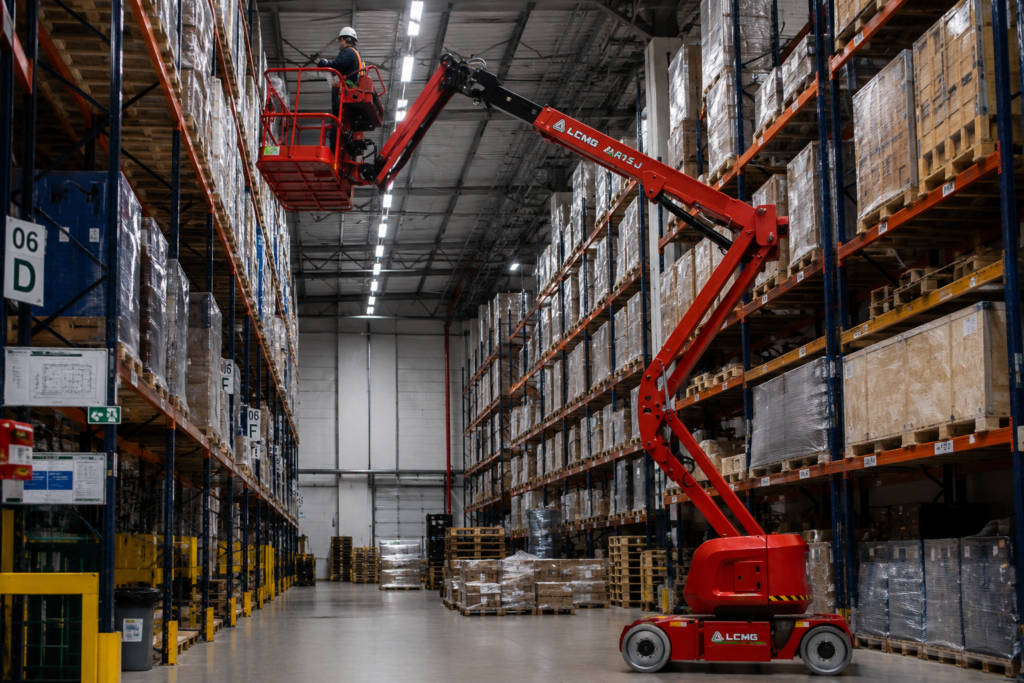 Plataforma articulada realiza manutenção e acesso a posições elevadas em centro de distribuição logístico.